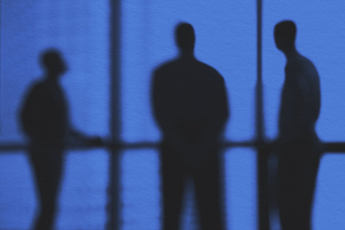 blurred silhouette image of 3 men standing by a window