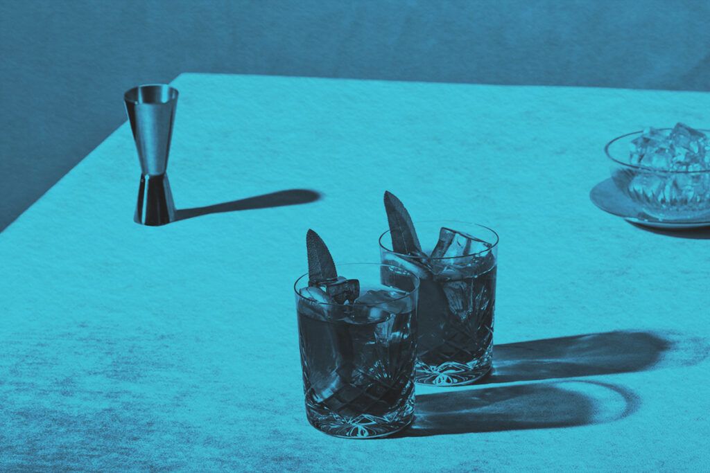 Two cocktails on counter with ice and a double jigger