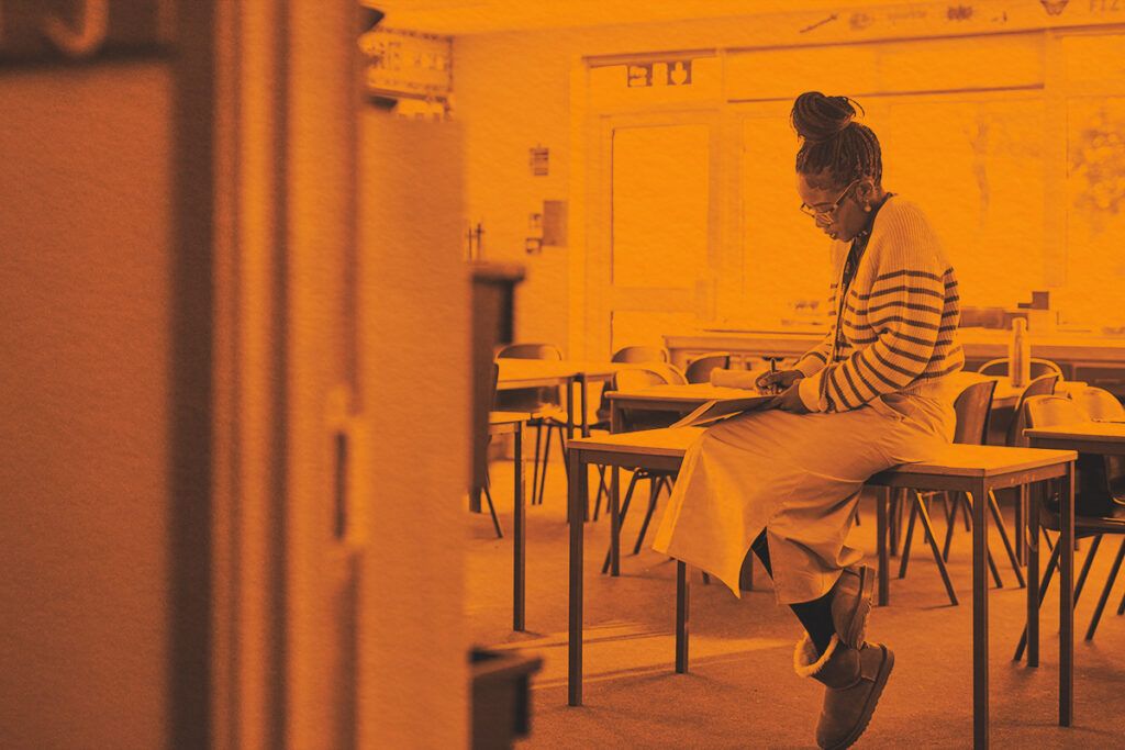 female teacher sitting on desk with classroom door open