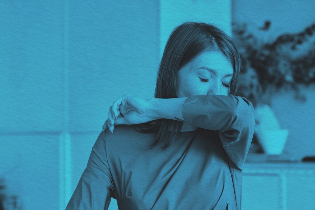 Woman covers mouth sneezing in office setting