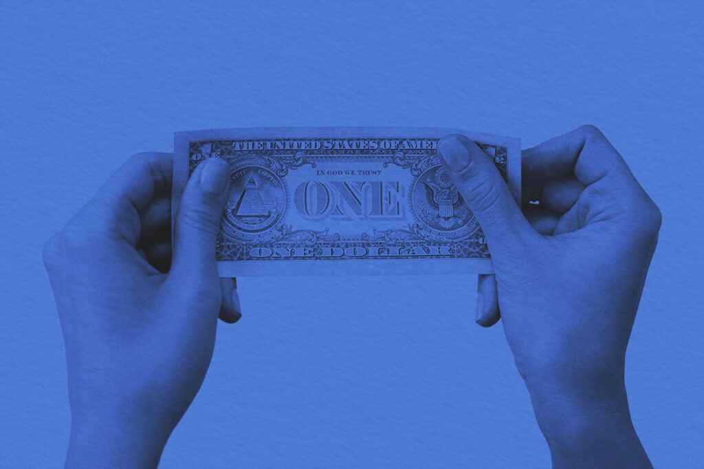 A close-up image of hands holding a one dollar bill