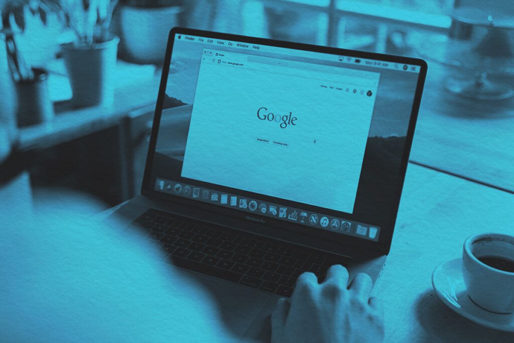 An adult using a laptop indoors, browsing Google at a wooden table with coffee