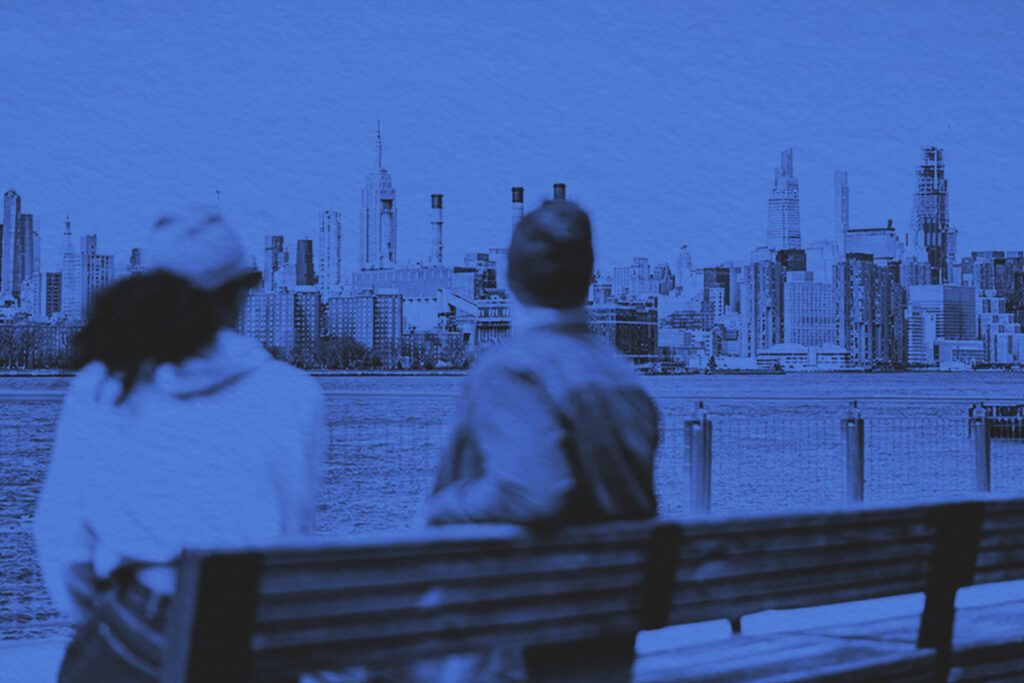 Two people sitting on an outdoor bench looking at Manhattan, New York City