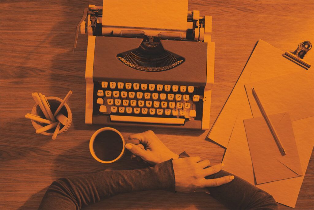 A person's hands holding a cup near a vintage typewriter
